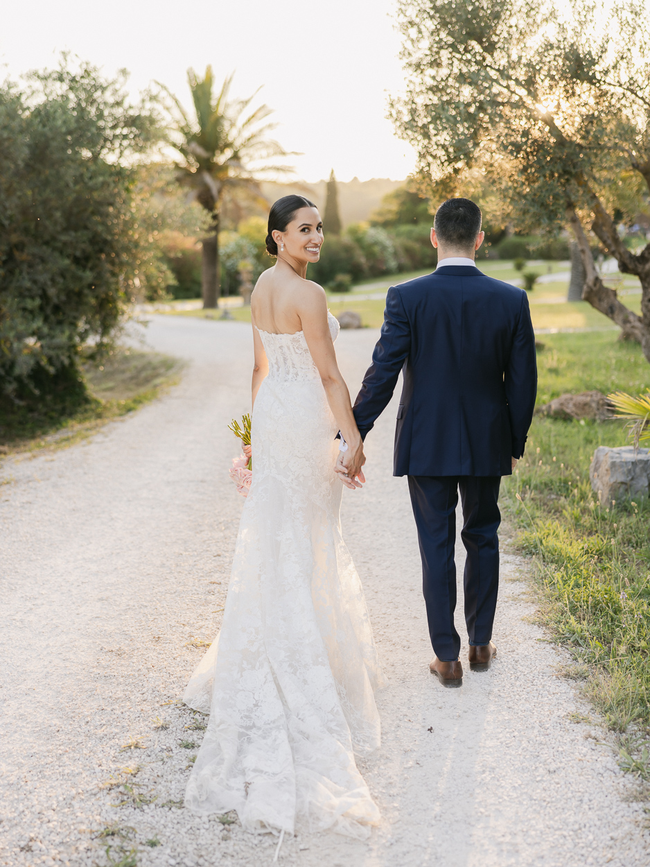 Bride looking back while walking through the olives groves with his groom at Chateau de la Roque Forcade